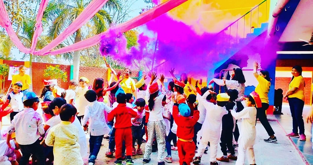 Children and staff celebrating Holi outdoors with colourful powder at Grandmaa's Preschool & DayCare, Greater Noida
